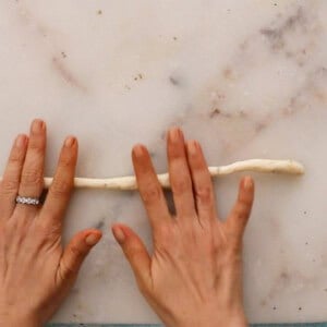 two hands rolling a white dough into a long rope.