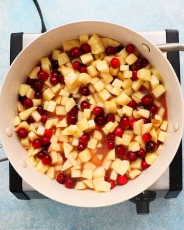 apple and cranberry pie filling cooking in a white pan.