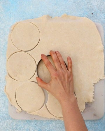 a hand cutting circles from a rolled pie crust.