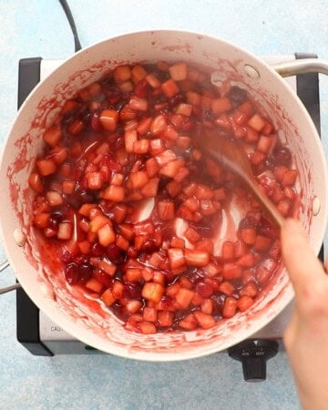 apple and cranberry pie filling cooking in a white pan.