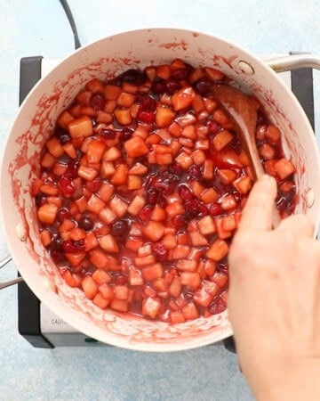 apple and cranberry pie filling cooking in a white pan.