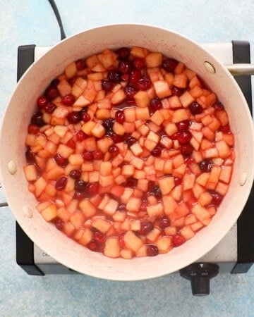 apple and cranberry pie filling cooking in a white pan.