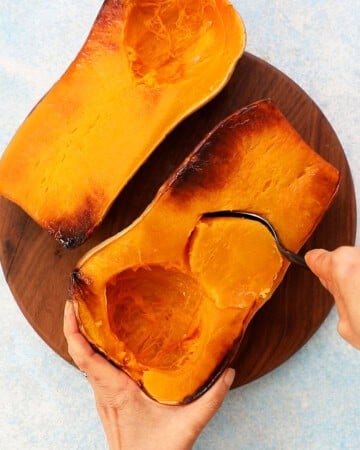 two roasted butternut squash halves on a wooden board.