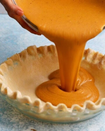 a hand pouring butternut squash pie filling into pie crust.