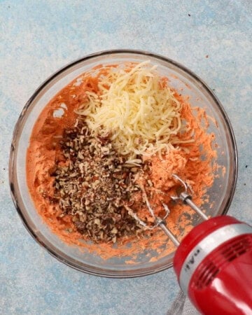 a red beater beating pink cheese ball mixture in a glass bowl.