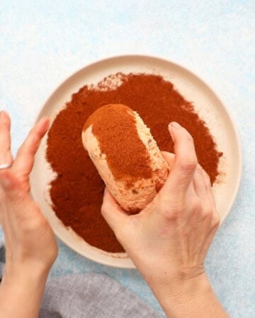 two hands rolling a pink cheese ball in paprika. 