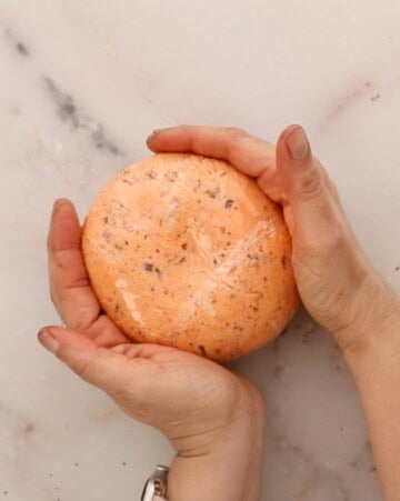 two hands shaping a tomato cheese ball.
