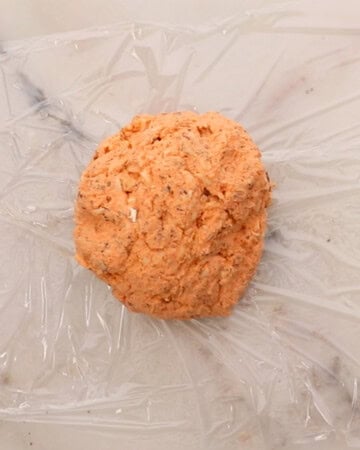 pink tomato cheese ball mixture in plastic wrap.