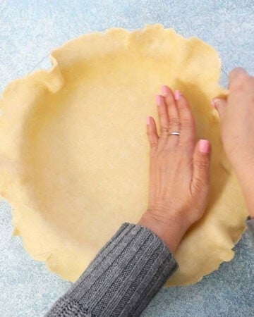 two hands shaping pie crust into a glass pie dish.