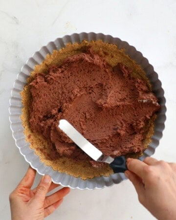 two hands spreading chocolate mousse in a tart pan.