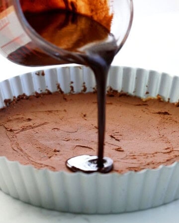 a hand pouring melted chocolate into a tart pan.