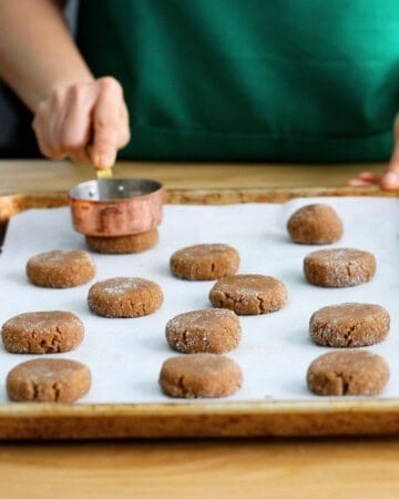 brown ginger molasses cookie dough balls in a white baking sheet.