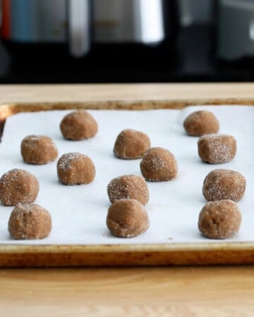 brown ginger molasses cookie dough balls in a white baking sheet.