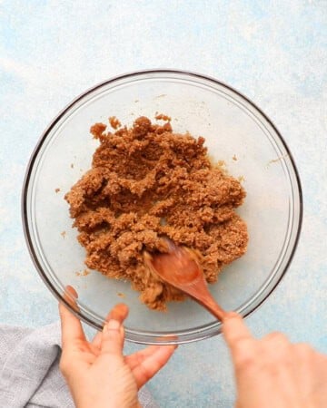a hand mixing ginger molasses cookie dough in a glass bowl.
