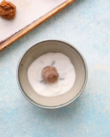 one cookie dough ball in a blue bowl with white sugar.