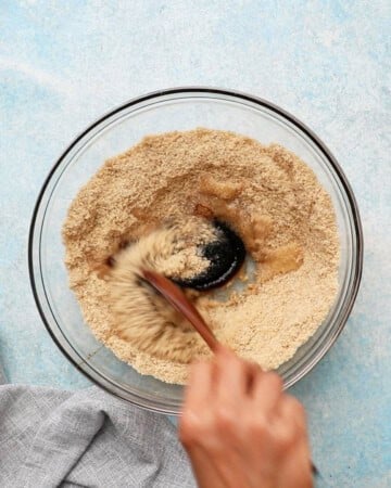 a hand mixing ginger molasses cookie dough in a glass bowl.