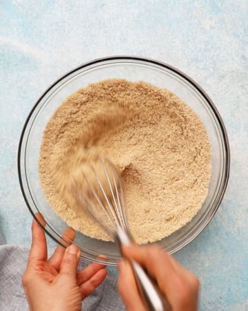 a hand whisking almond flour, brown sugar and spices in a glass bowl.