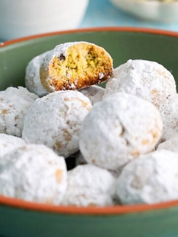 almond flour pistachio snowball cookies in a green bowl.