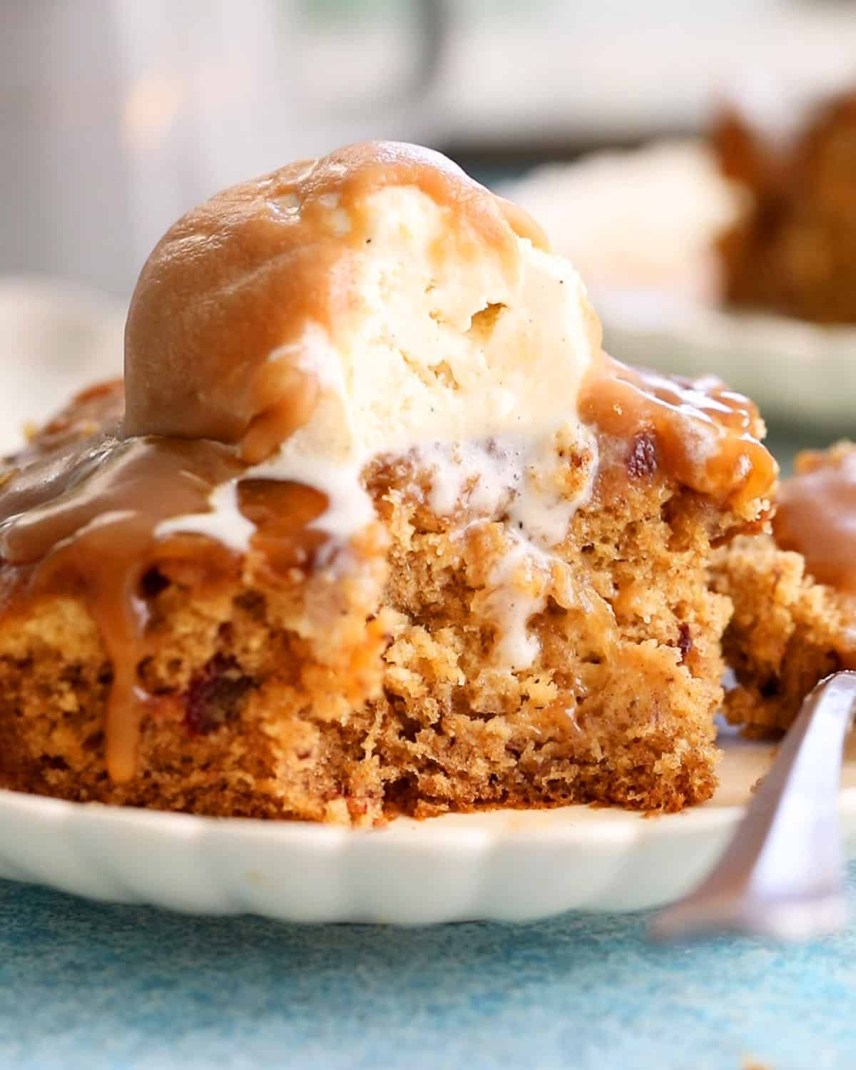 one slice of brown date pudding topped with white ice cream in a white plate.