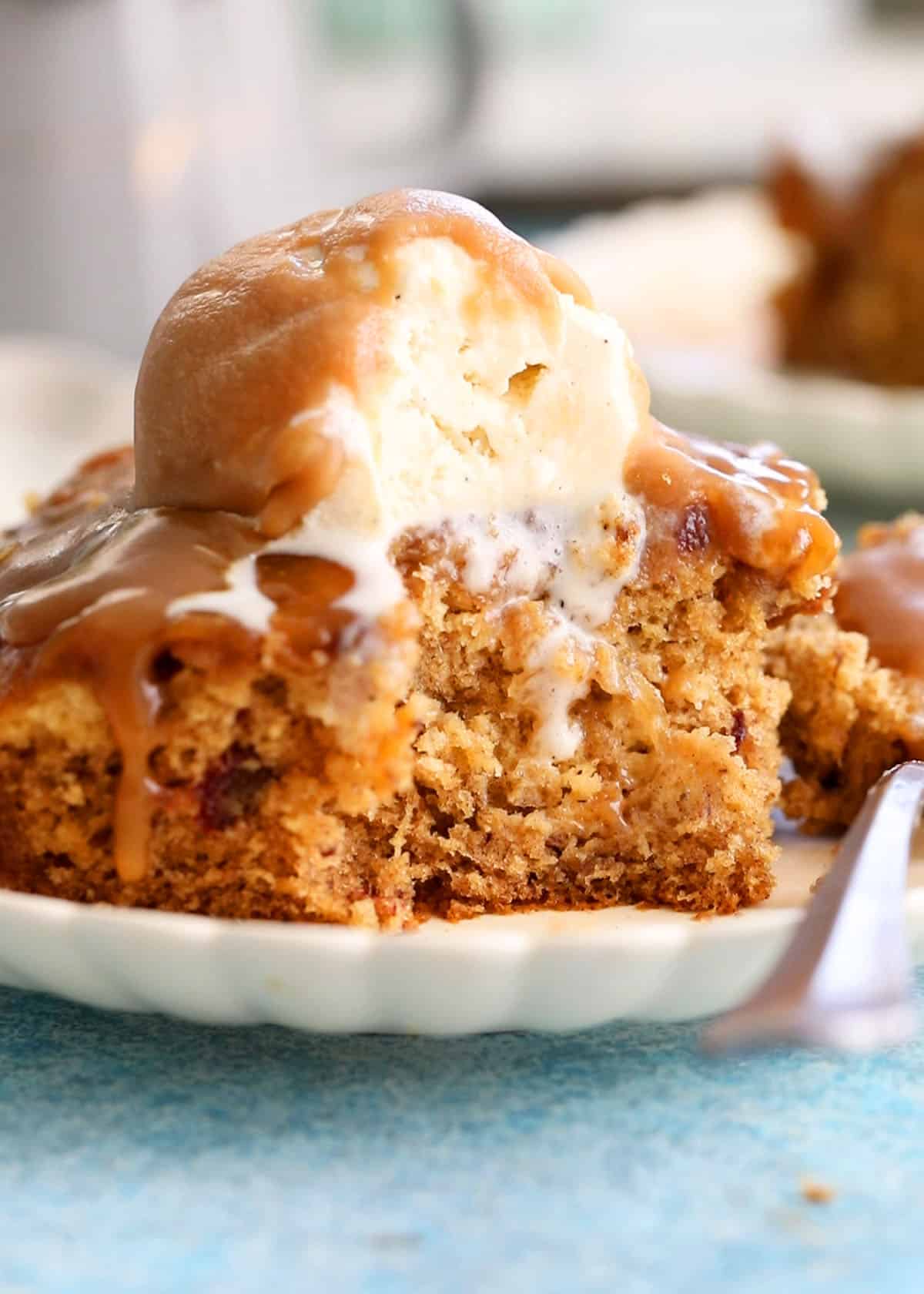 one slice of brown date pudding topped with white ice cream in a white plate.