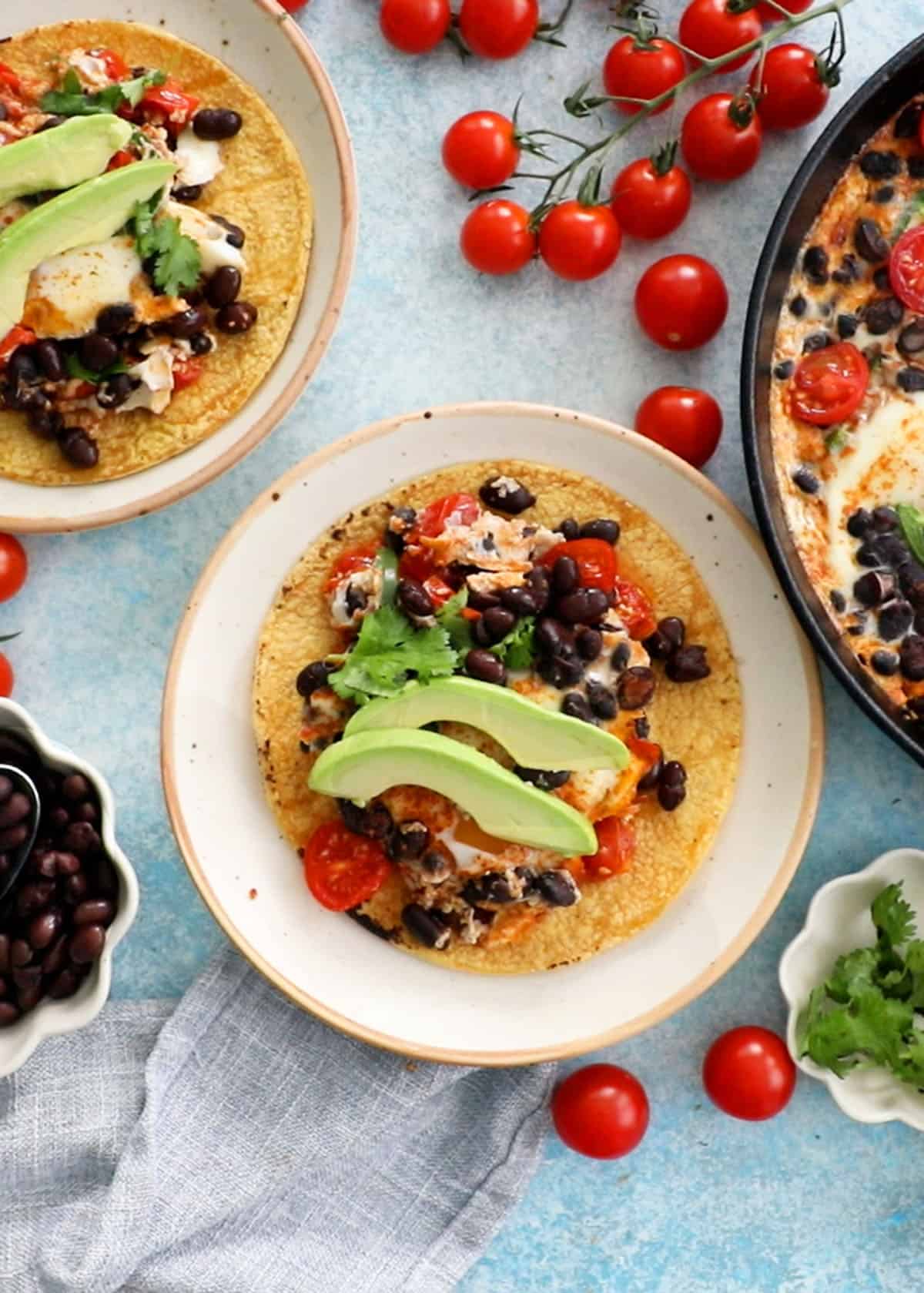 baked eggs, red tomato, black beans and green avocado in a yellow tortilla.
