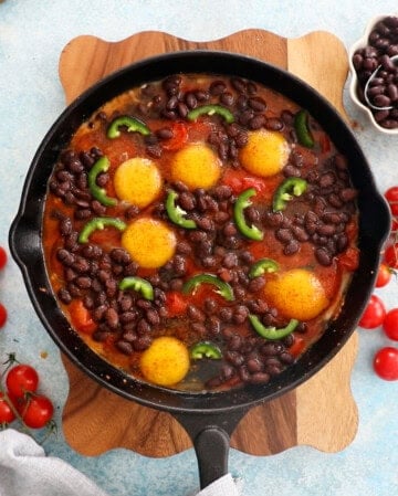 red cherry tomatoes, black beans and eggs in a black skillet.