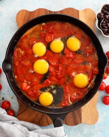 red cherry tomatoes and eggs in a black skillet.