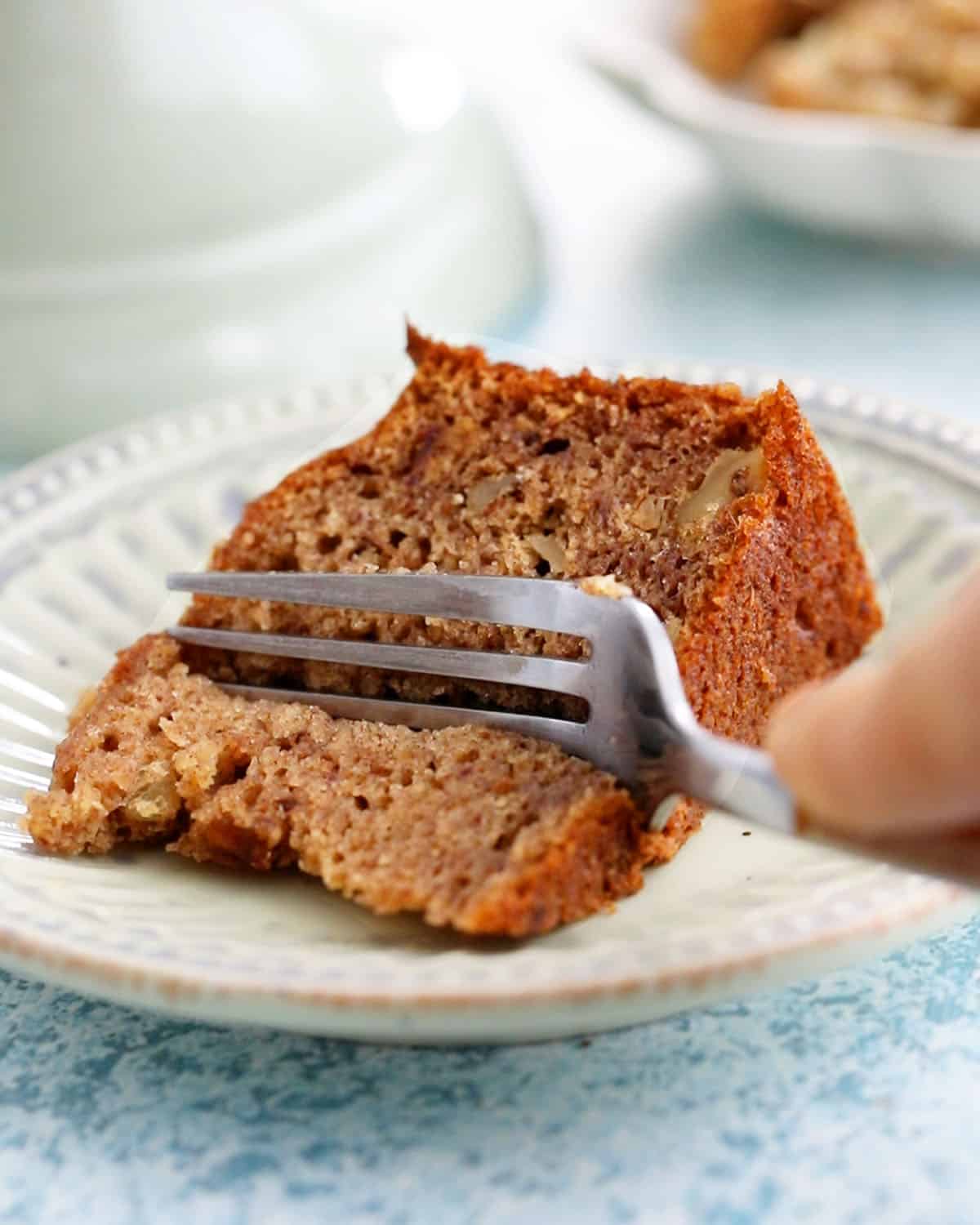 one slice of brown date cake in a green plate along with a fork.