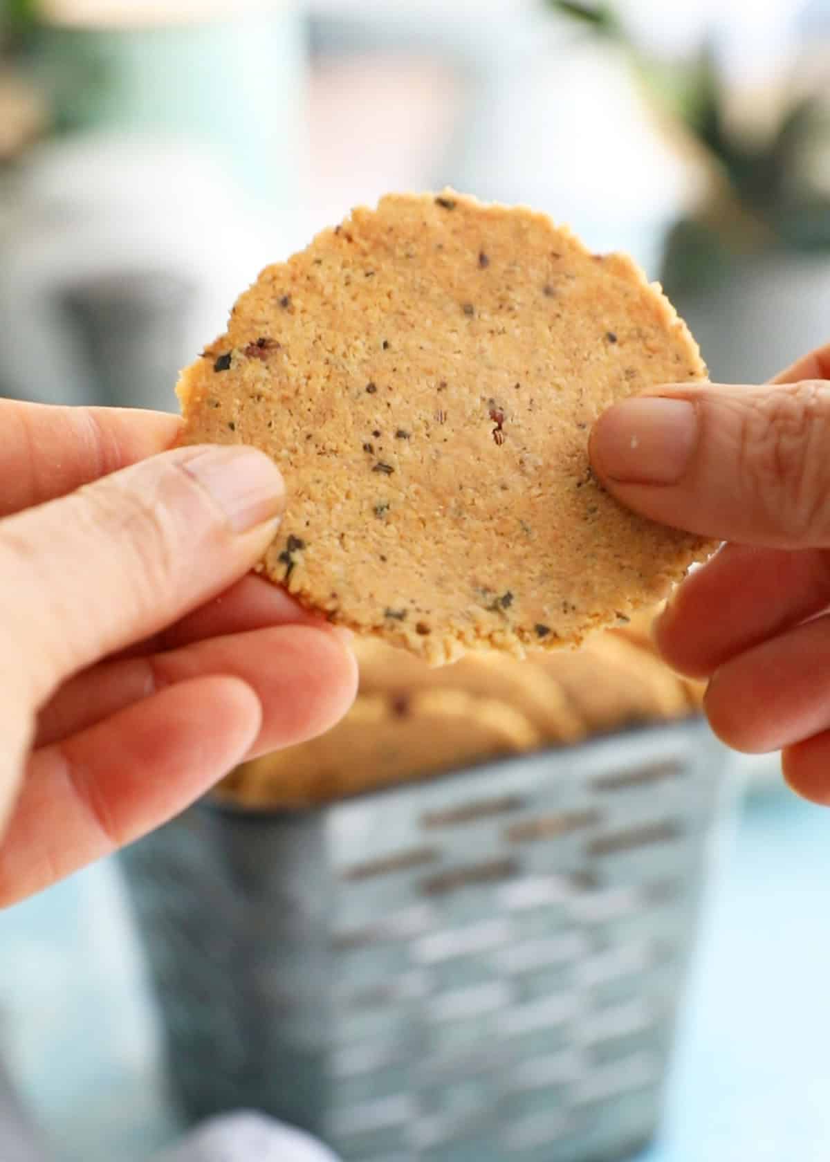 two hands holding one round almond flour cracker.