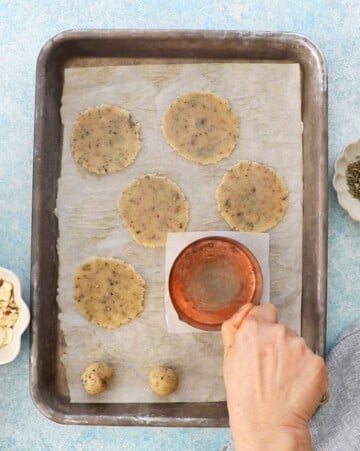 two hands flattening almond flour crackers in a metal baking sheet.
