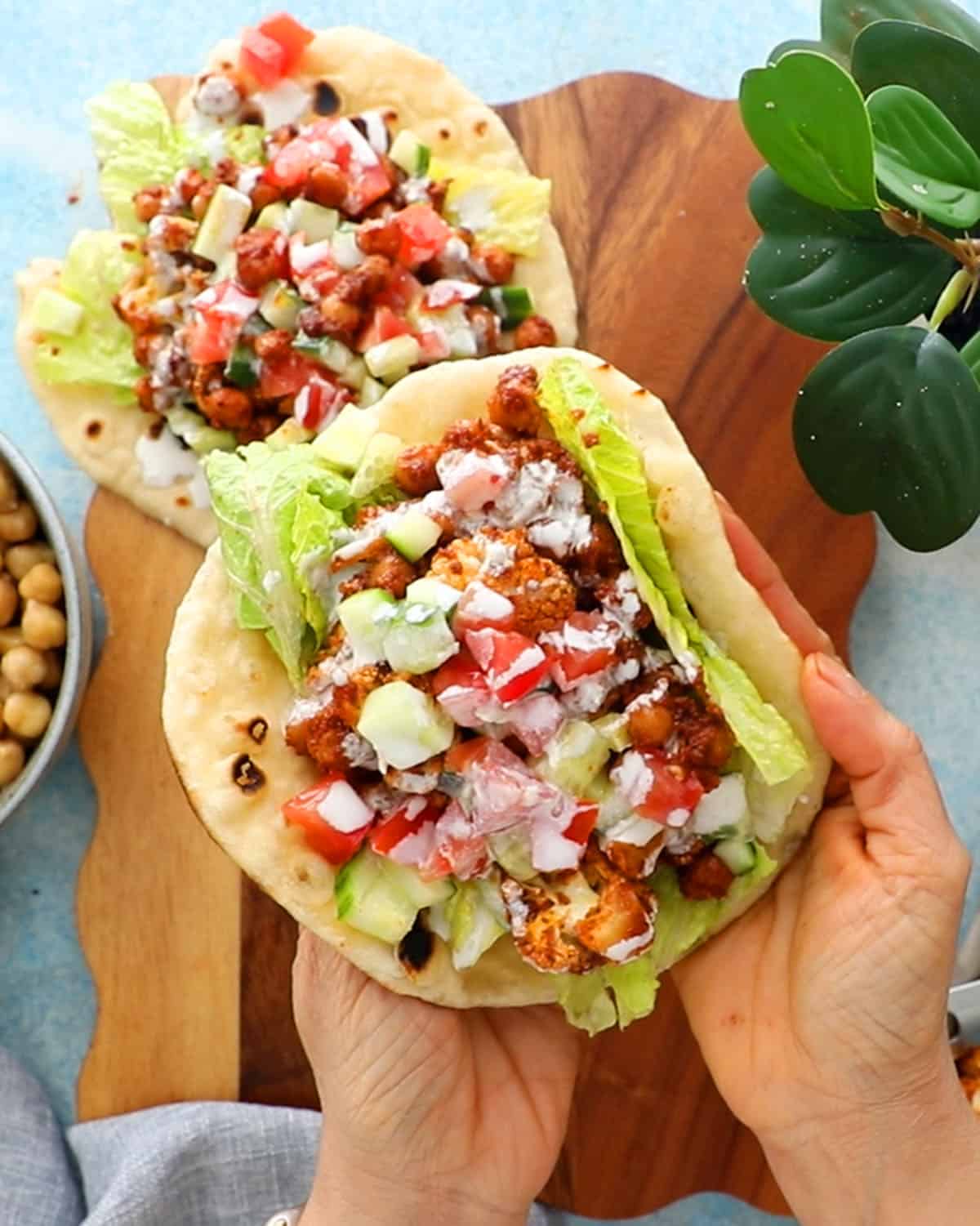 two hands holding one chickpea and cauliflower wrap.