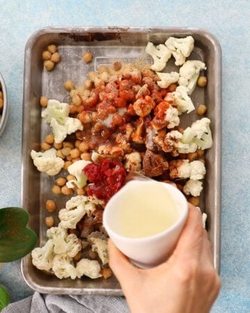 a hand pouring oil into a metal sheet pan.