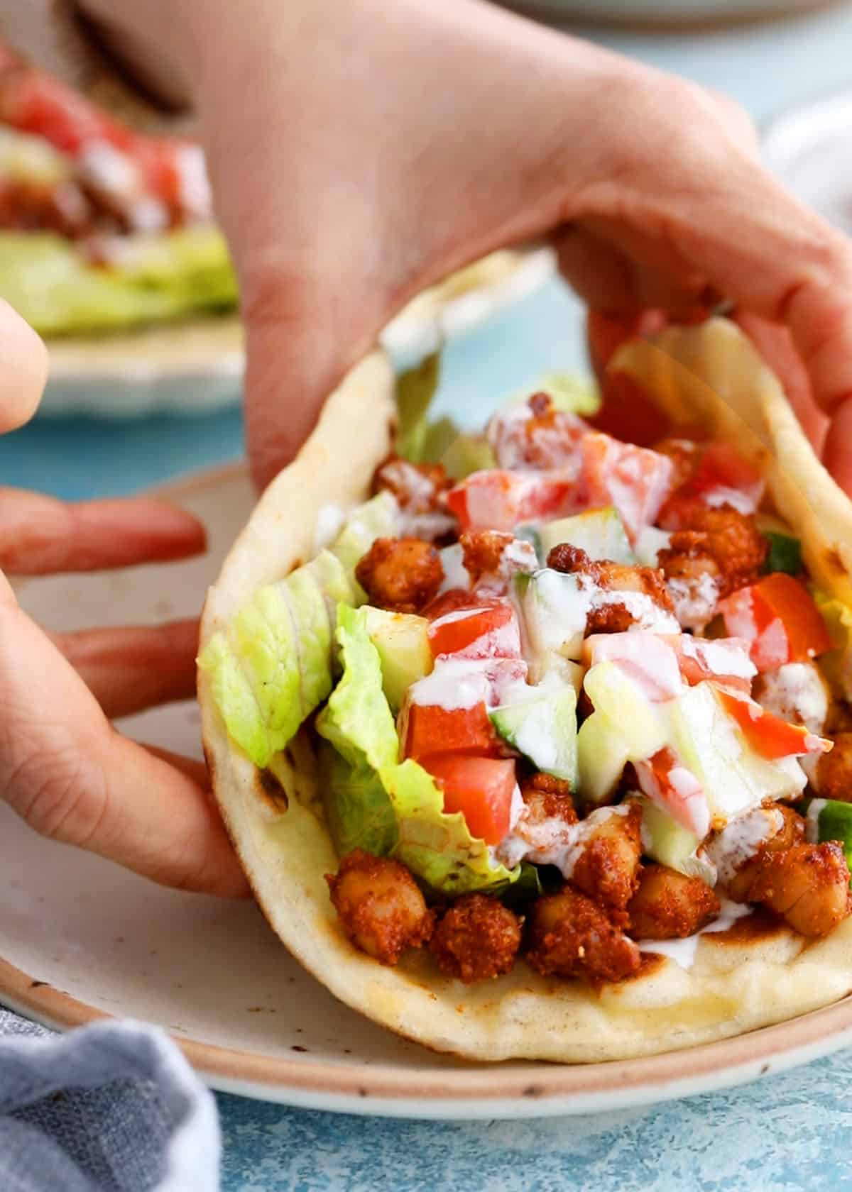 two hands holding one chickpeas and cauliflower wrap.