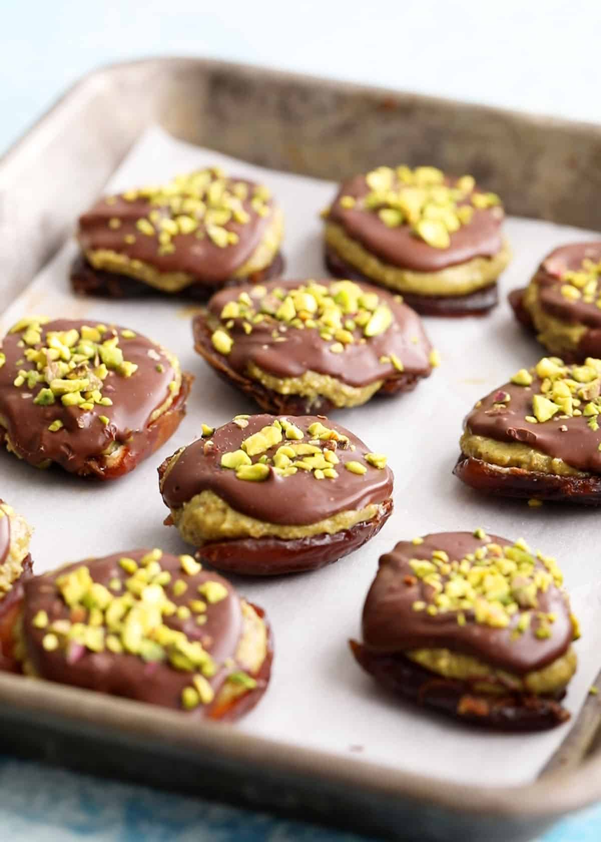 brown and green date chocolate pistachio bites on a metal sheet pan.
