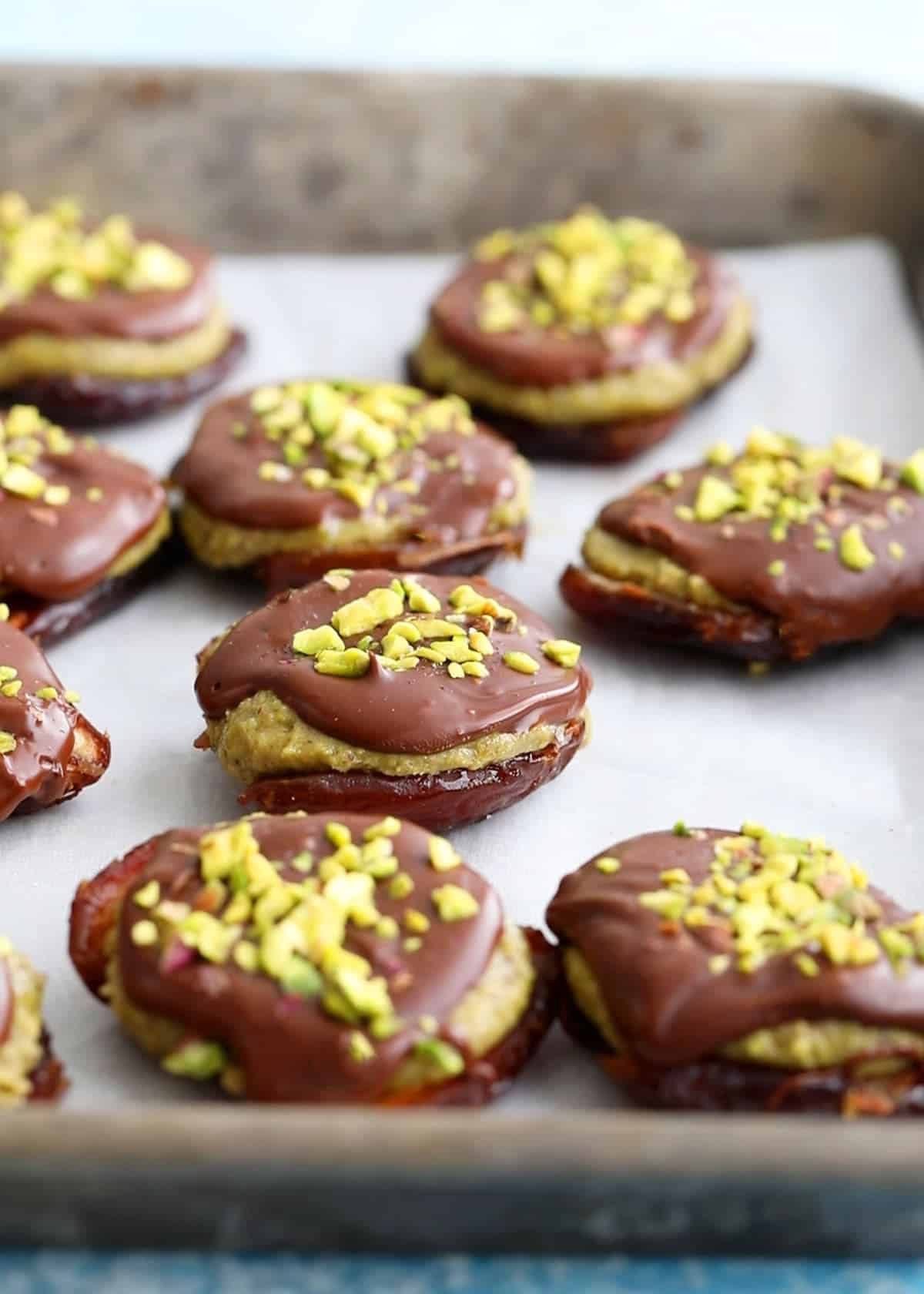 brown and green date chocolate pistachio bites on a metal sheet pan.