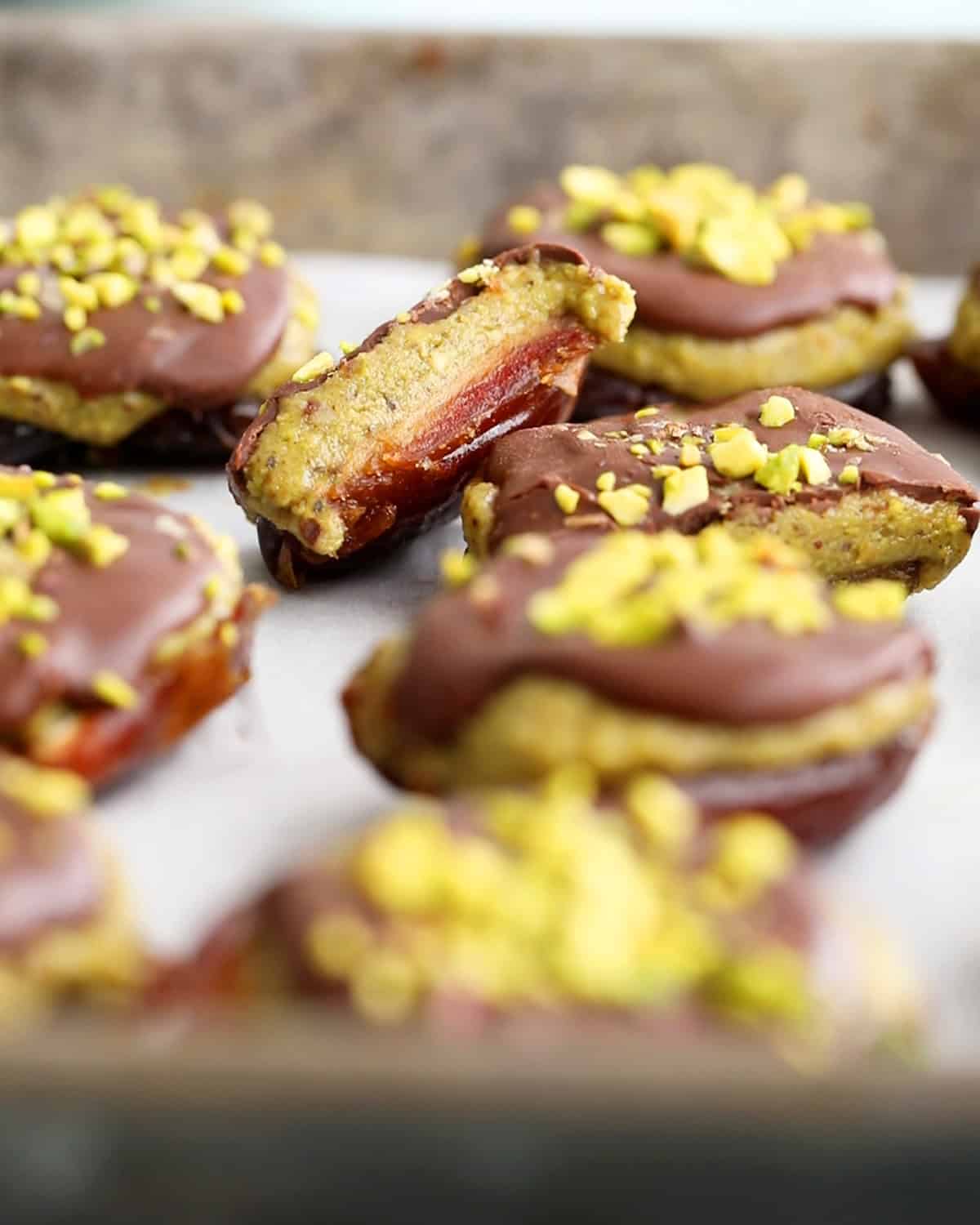 brown and green date chocolate pistachio bites on a metal sheet pan.