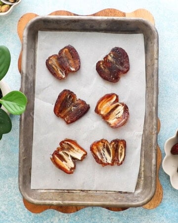 6 brown dates in a metal sheet pan.