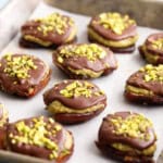 brown and green chocolate pistachio date bites on a metal baking sheet.