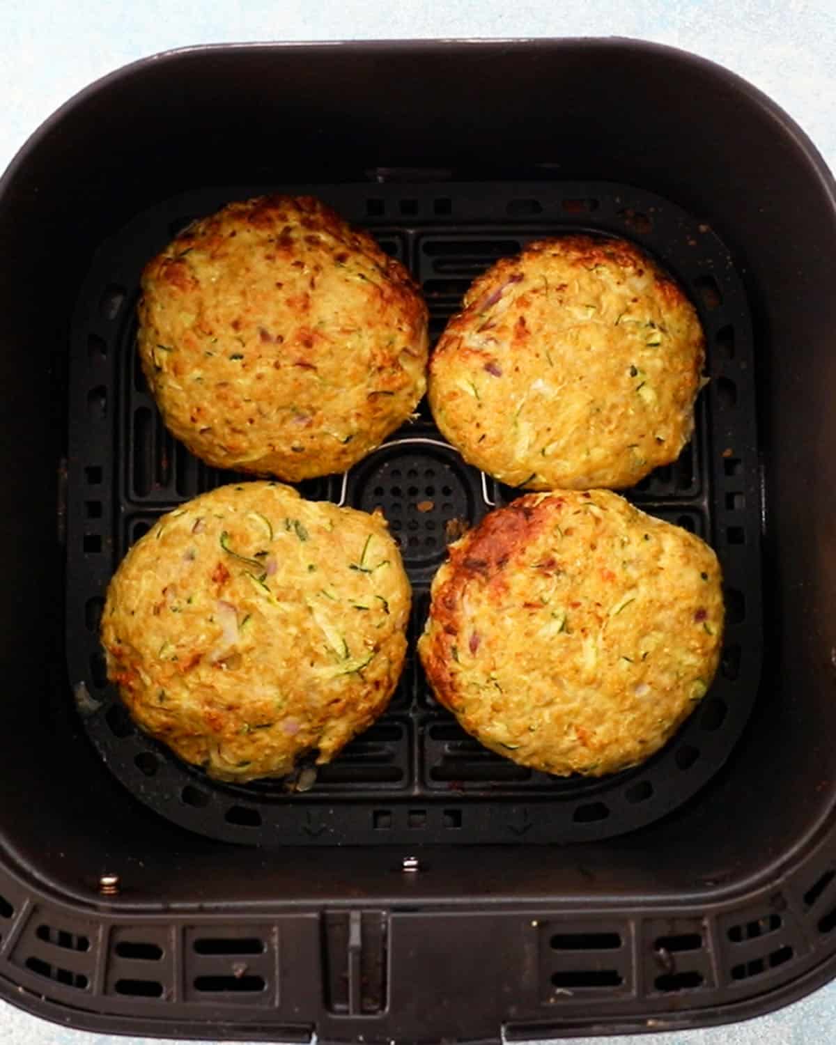 4 chicken zucchini burger patties in a black air fryer basket.