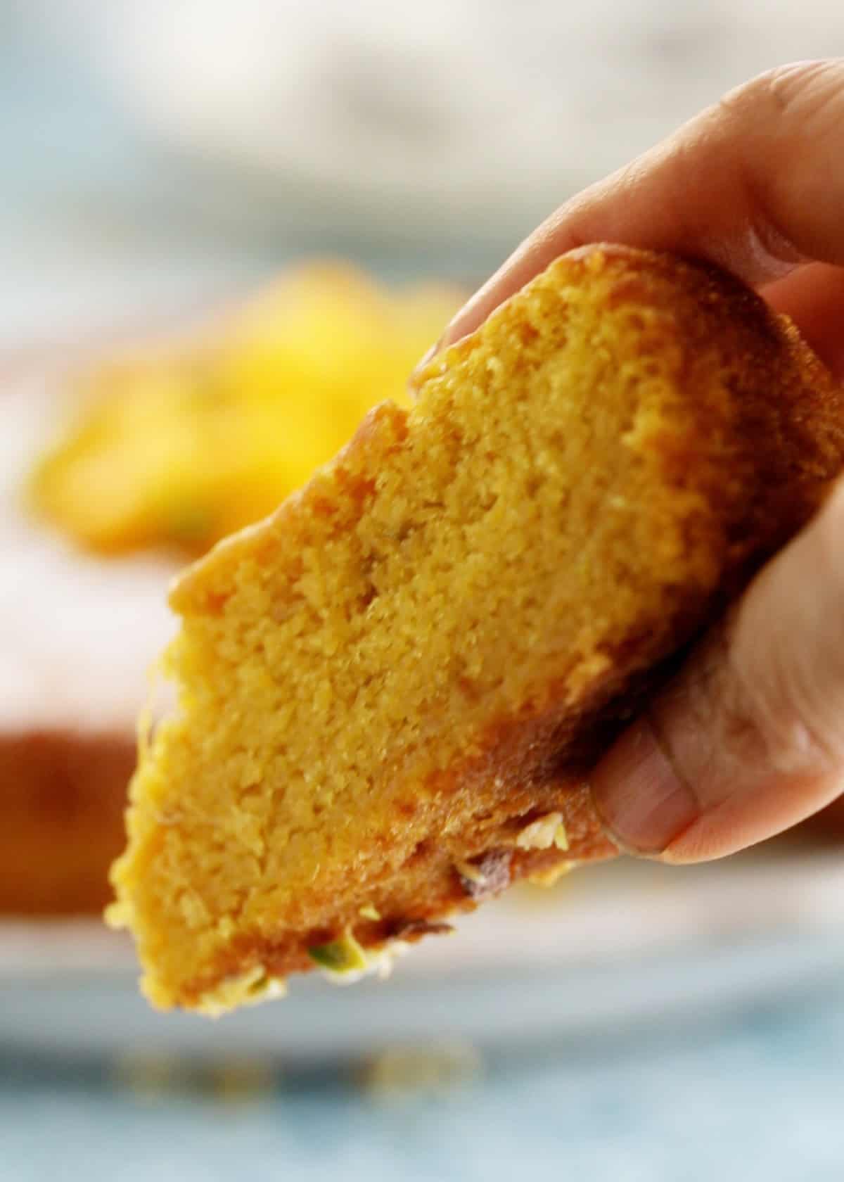 a hand holding one slice of yellow mango cake.