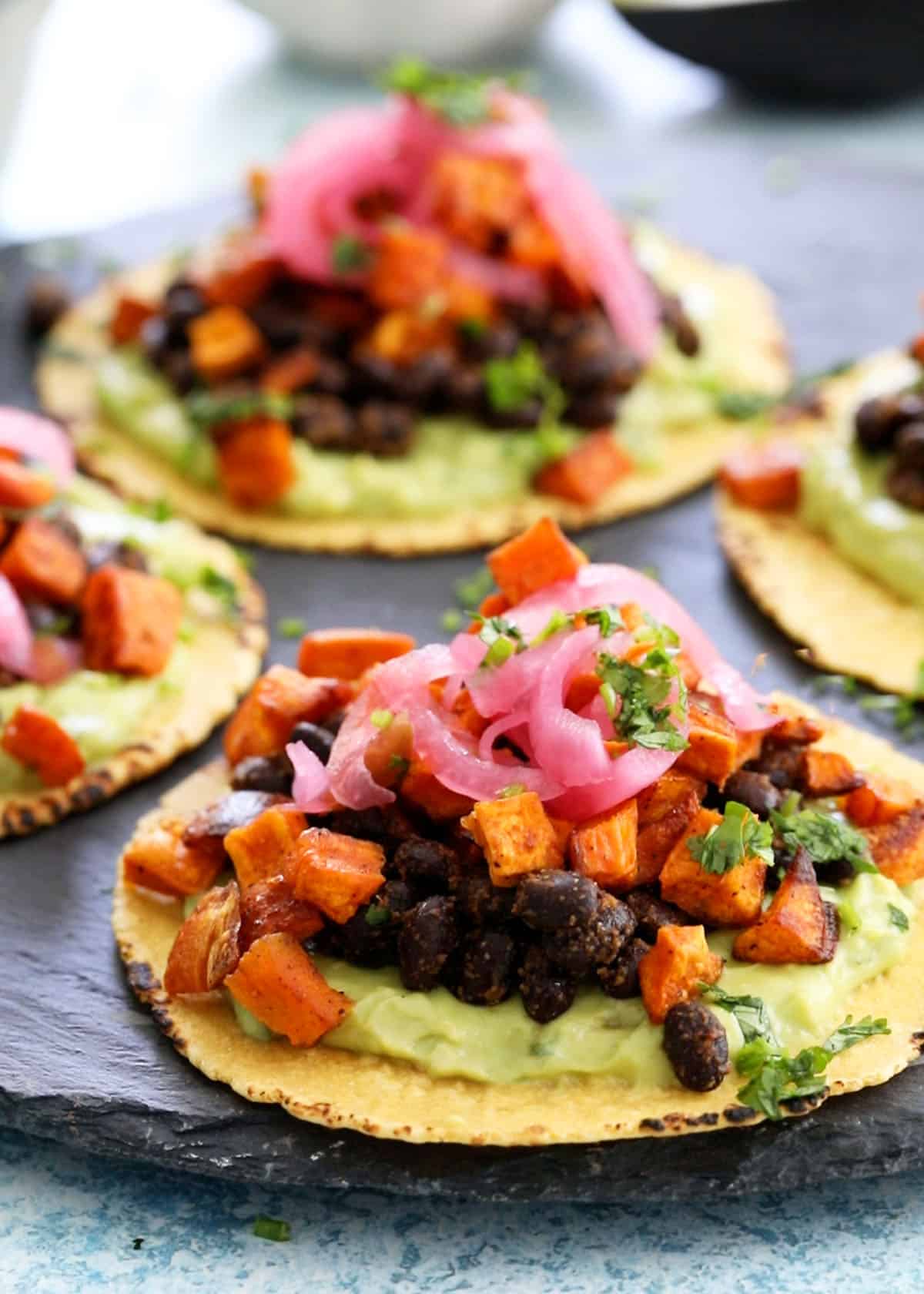 3 sweet potato and black bean tacos on a black platter.