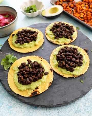 4 sweet potato and black bean tacos on a black platter.