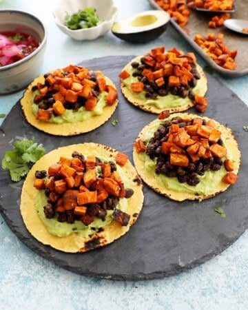 4 sweet potato and black bean tacos on a black platter.