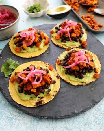 4 sweet potato and black bean tacos on a black platter.