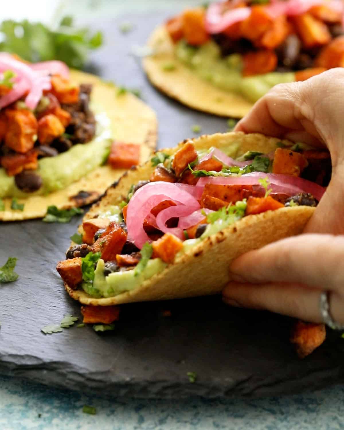 3 sweet potato and black bean tacos on a black platter.
