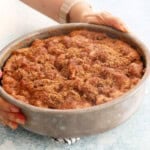 two hands holding a metal pan with brown apple cake.