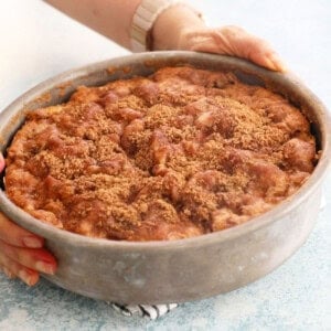 two hands holding a metal pan with brown apple cake.