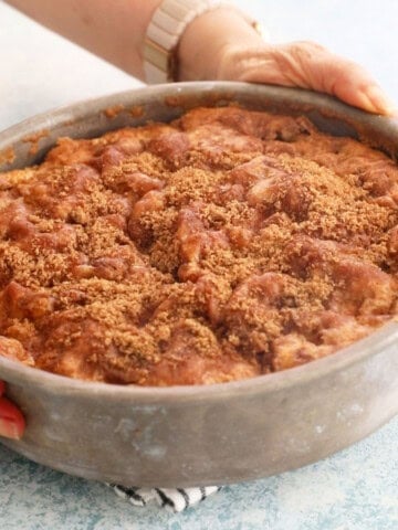 two hands holding a metal pan with brown apple cake.