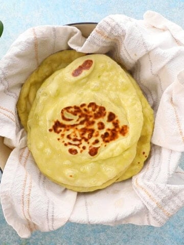 green colored naan stacked in a white cloth.