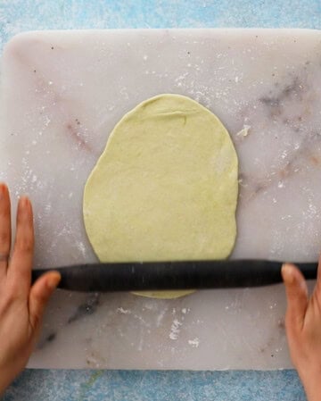 two hand rolling a piece of naan dough.
